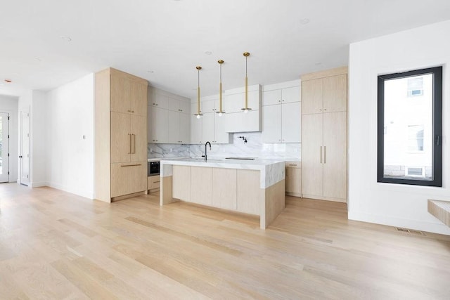 1597 Centre St Unit A, Newton, MA 02461 - kitchen featuring light wood-type flooring, light brown cabinetry, light countertops, backsplash, and a large island with sink