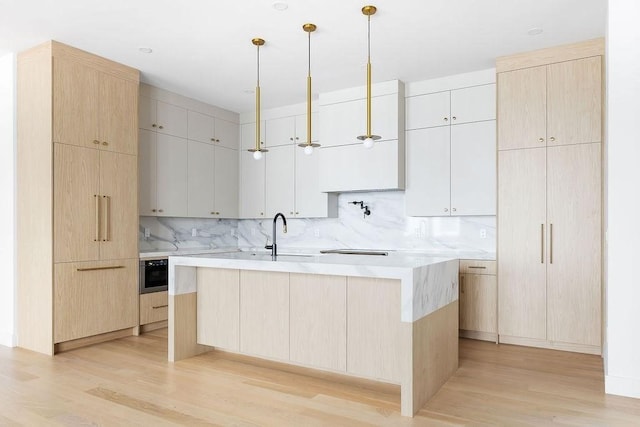 1597 Centre St Unit A, Newton, MA 02461 - kitchen featuring light wood finished floors, light countertops, backsplash, a center island with sink, and light brown cabinets
