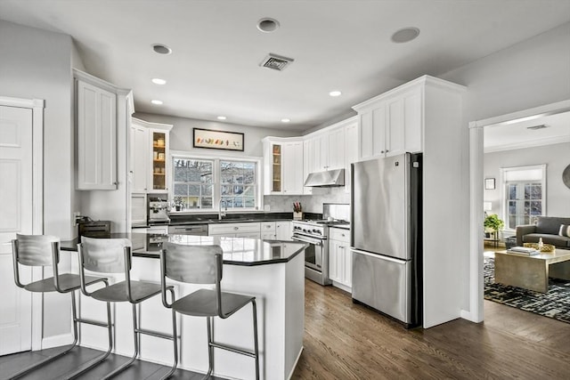 kitchen with visible vents, a peninsula, under cabinet range hood, appliances with stainless steel finishes, and dark countertops