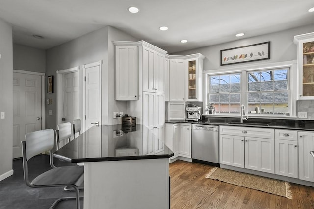 kitchen with a sink, dark countertops, wood finished floors, white cabinets, and dishwasher