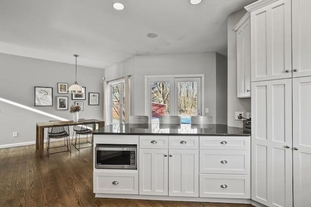 kitchen featuring stainless steel microwave, dark countertops, white cabinets, and dark wood finished floors