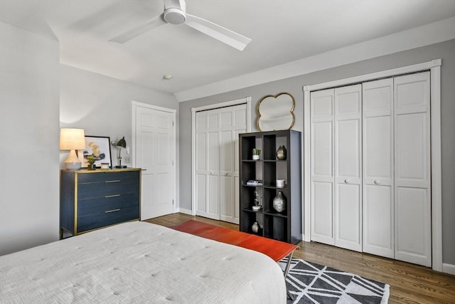 bedroom with baseboards, two closets, dark wood finished floors, and a ceiling fan