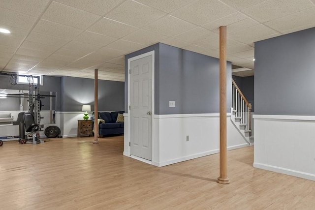 basement with stairway, a paneled ceiling, a wainscoted wall, and wood finished floors