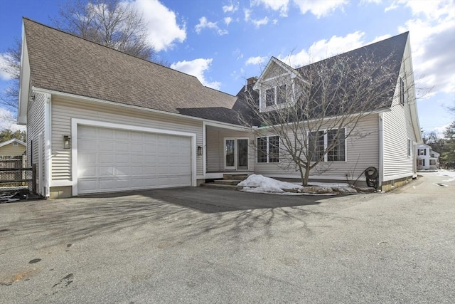 new england style home featuring aphalt driveway, a garage, and roof with shingles