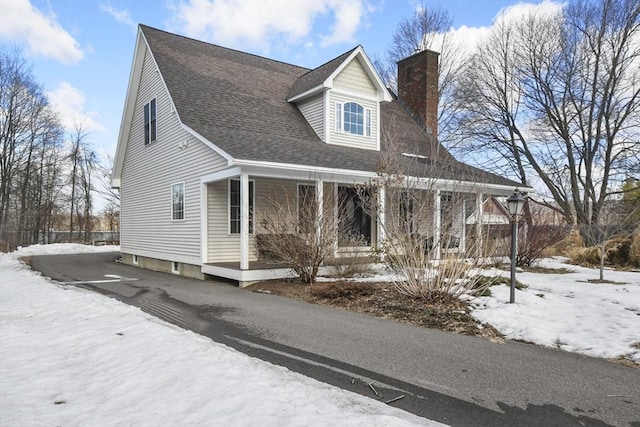 view of front of house featuring a porch, a chimney, driveway, and roof with shingles