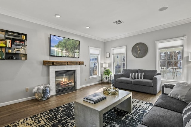 living area featuring visible vents, a brick fireplace, crown molding, baseboards, and wood finished floors