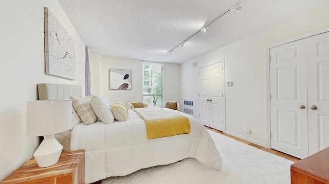 99 Pond Ave Unit 326, Brookline, MA 02445 - bedroom featuring a textured ceiling, track lighting, radiator heating unit, and wood finished floors