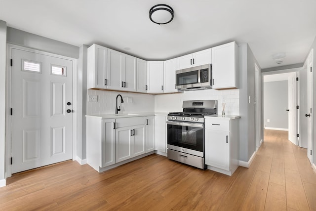 kitchen featuring white cabinetry, sink, stainless steel appliances, backsplash, and light hardwood / wood-style floors