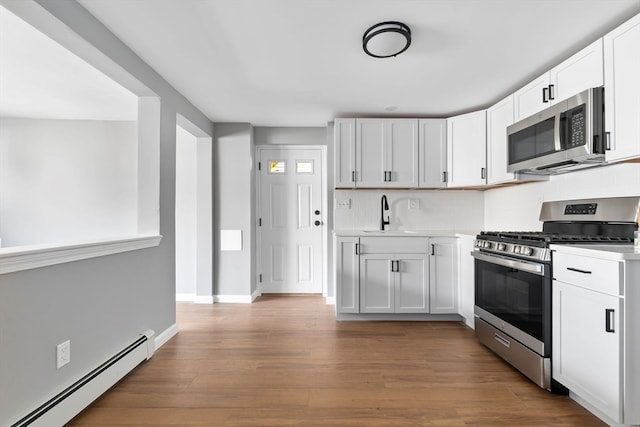 kitchen with sink, white cabinetry, baseboard heating, and appliances with stainless steel finishes