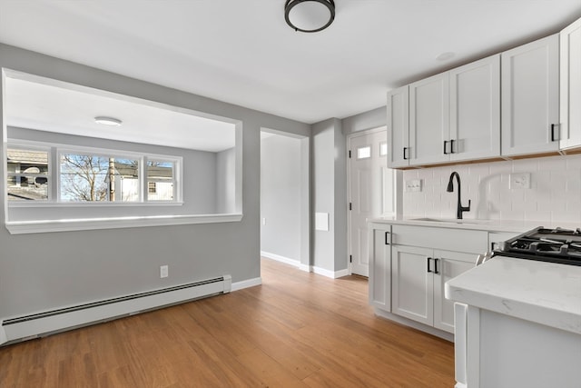 kitchen with white cabinets, light wood-type flooring, a baseboard heating unit, and sink