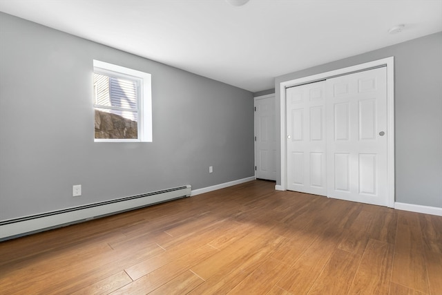 unfurnished bedroom featuring a closet, wood-type flooring, and a baseboard heating unit