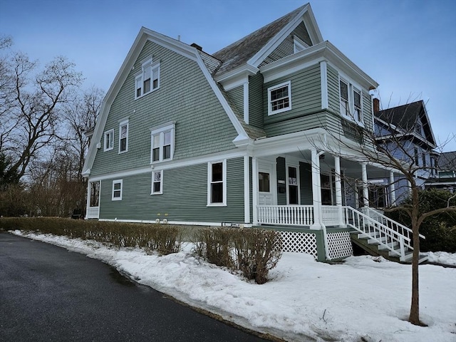 snow covered property with covered porch, roof with shingles, and a gambrel roof