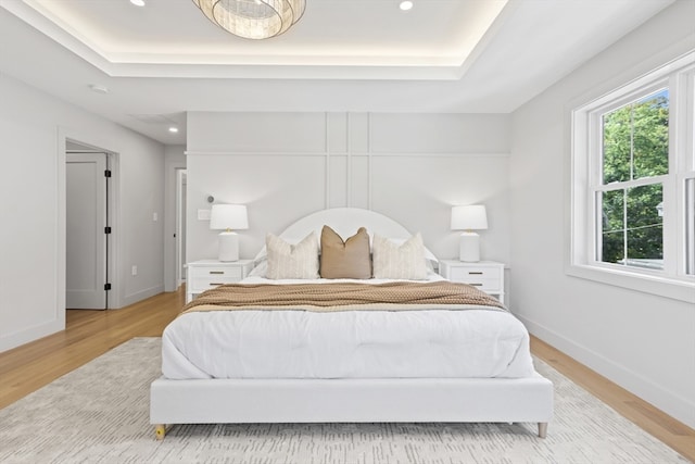 bedroom with light hardwood / wood-style floors and a raised ceiling