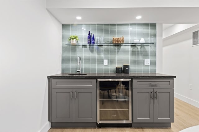 bar featuring gray cabinetry, wine cooler, dark stone counters, light wood-type flooring, and sink