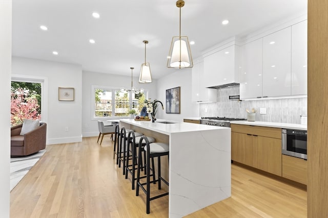 kitchen featuring light hardwood / wood-style flooring, hanging light fixtures, sink, white cabinets, and a kitchen island with sink