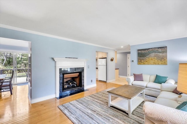 living room with ornamental molding, baseboards, recessed lighting, a high end fireplace, and light wood-style flooring