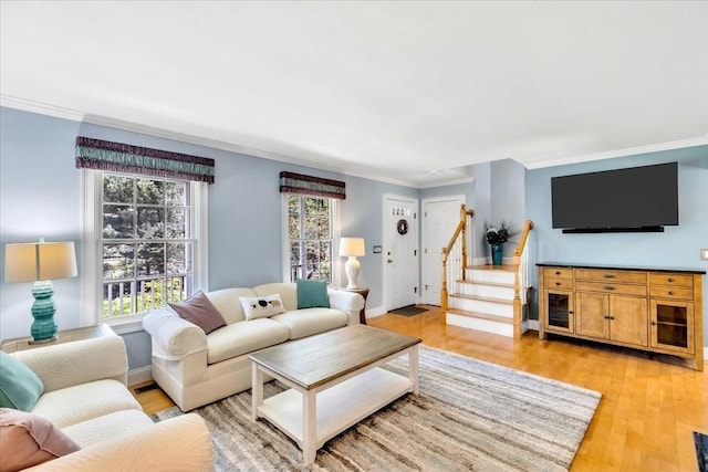 living area with crown molding, baseboards, light wood-style floors, and stairs