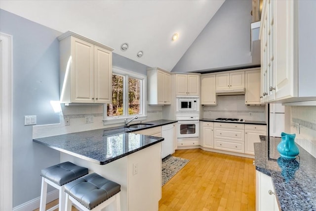 kitchen featuring a sink, white appliances, a peninsula, backsplash, and under cabinet range hood