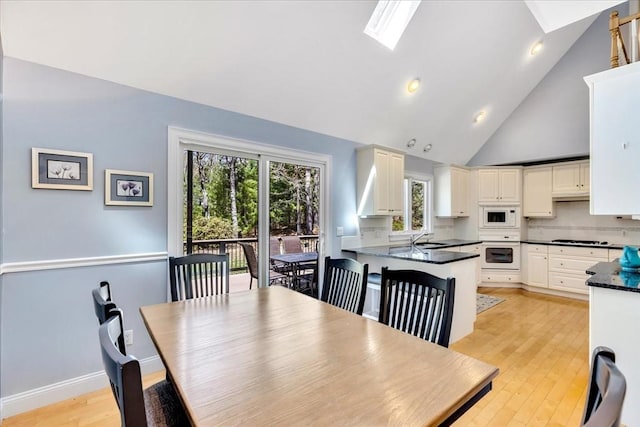 dining space featuring baseboards, high vaulted ceiling, light wood-type flooring, recessed lighting, and a skylight