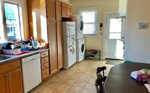562 Main, Medford, MA 02155 - kitchen featuring white appliances, stacked washing machine and dryer, light tile patterned floors, and brown cabinetry