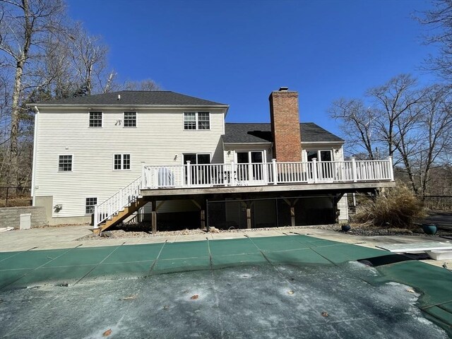 back of property with a deck, stairs, a covered pool, and a chimney