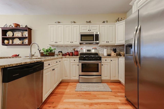 kitchen with light wood-type flooring, light stone counters, stainless steel appliances, and sink