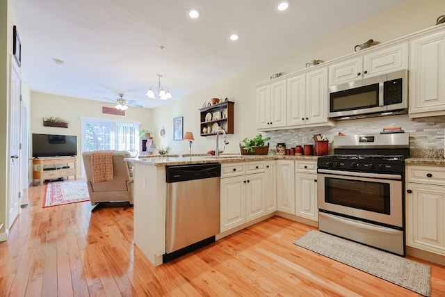 kitchen featuring light wood-type flooring, stainless steel appliances, decorative light fixtures, kitchen peninsula, and light stone countertops