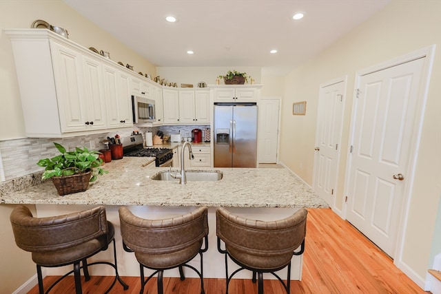 kitchen with white cabinets, light hardwood / wood-style flooring, stainless steel appliances, sink, and a kitchen breakfast bar