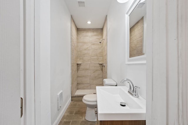 bathroom with toilet, a tile shower, and vanity