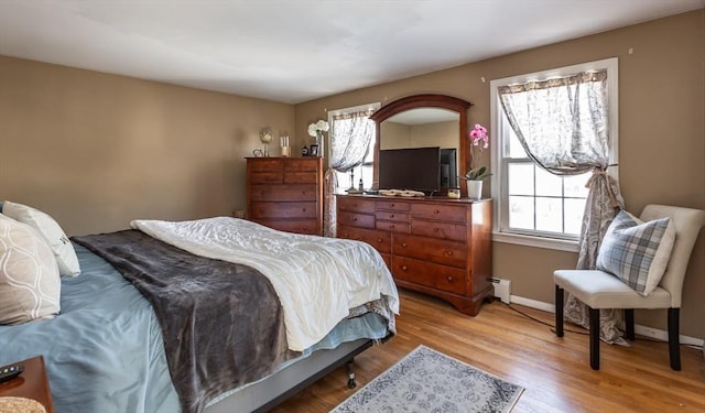 bedroom featuring a baseboard heating unit, wood finished floors, and baseboards