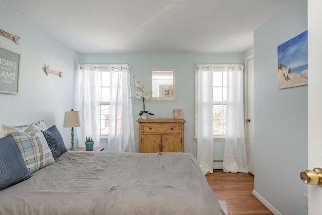 bedroom featuring baseboards, multiple windows, a baseboard heating unit, and wood finished floors