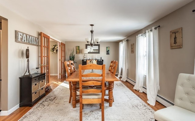 dining space featuring a chandelier, a baseboard radiator, baseboards, and light wood finished floors