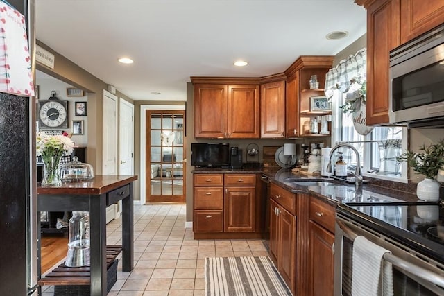 kitchen featuring open shelves, light tile patterned floors, appliances with stainless steel finishes, a sink, and dark stone counters