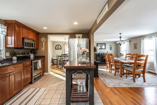 kitchen with a chandelier, a sink, appliances with stainless steel finishes, brown cabinetry, and decorative light fixtures