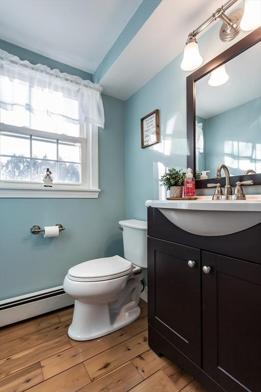 half bathroom featuring vanity, a baseboard radiator, wood finished floors, and toilet