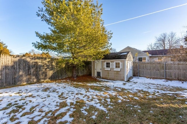 yard covered in snow with a fenced backyard, an outdoor structure, and a storage unit