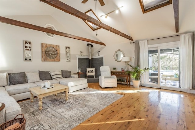 living room featuring a wood stove, ceiling fan, wood finished floors, high vaulted ceiling, and beamed ceiling