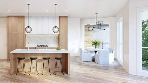 kitchen with light hardwood / wood-style flooring, hanging light fixtures, and a kitchen island with sink