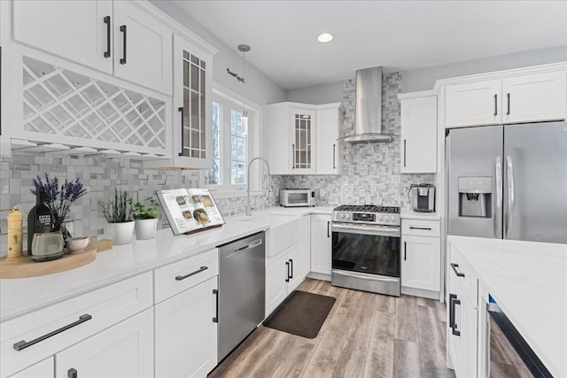 kitchen with white cabinetry, wall chimney range hood, backsplash, light hardwood / wood-style floors, and appliances with stainless steel finishes