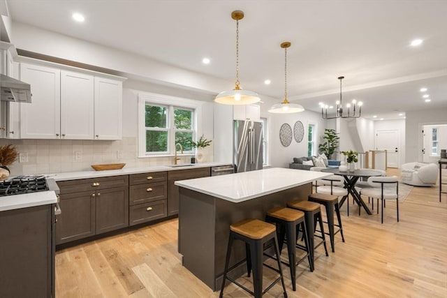 kitchen with appliances with stainless steel finishes, sink, pendant lighting, light hardwood / wood-style flooring, and white cabinets