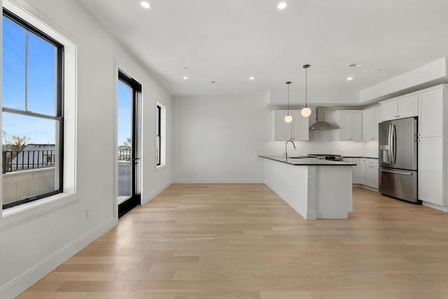 kitchen with white cabinetry, wall chimney range hood, stainless steel fridge with ice dispenser, kitchen peninsula, and pendant lighting