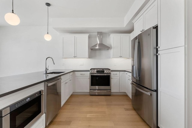 kitchen featuring pendant lighting, wall chimney range hood, sink, appliances with stainless steel finishes, and white cabinetry