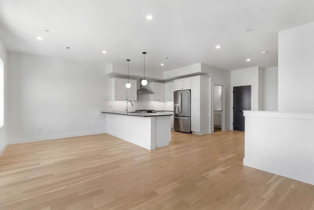 kitchen with white cabinets, wall chimney range hood, stainless steel refrigerator with ice dispenser, decorative light fixtures, and light hardwood / wood-style floors