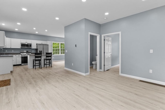 67 Elliott Ave, Dracut, MA 01826 - kitchen featuring appliances with stainless steel finishes, white cabinetry, a kitchen island, a breakfast bar, and light wood finished floors