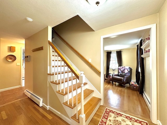 staircase featuring baseboard heating, wood-type flooring, and a textured ceiling