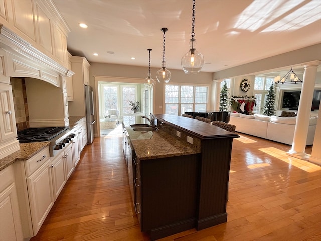 kitchen featuring sink, stainless steel appliances, hanging light fixtures, light hardwood / wood-style flooring, and an island with sink