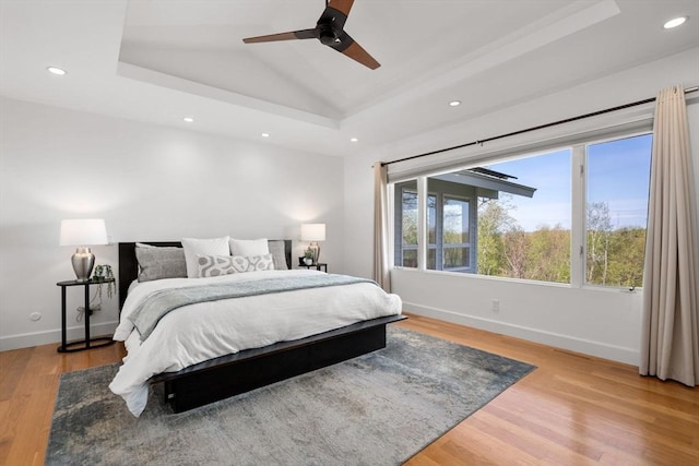 bedroom featuring a raised ceiling, baseboards, recessed lighting, and light wood-style floors