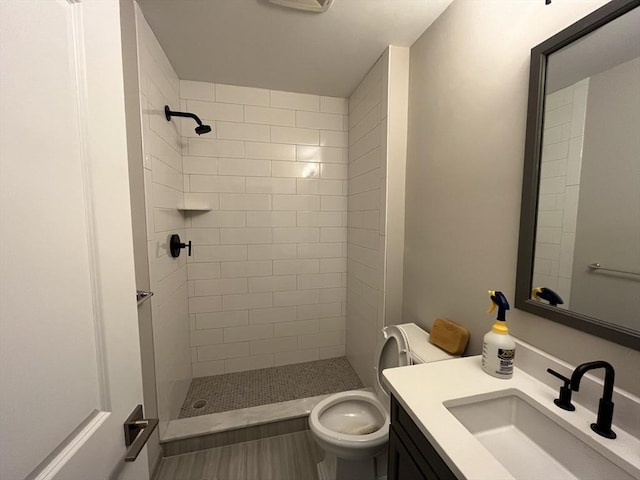 full bathroom featuring a tile shower, toilet, and vanity