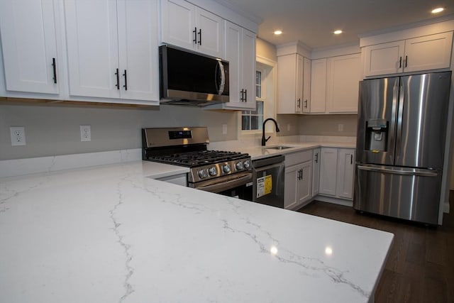 kitchen with appliances with stainless steel finishes, white cabinetry, sink, light stone counters, and dark wood-type flooring