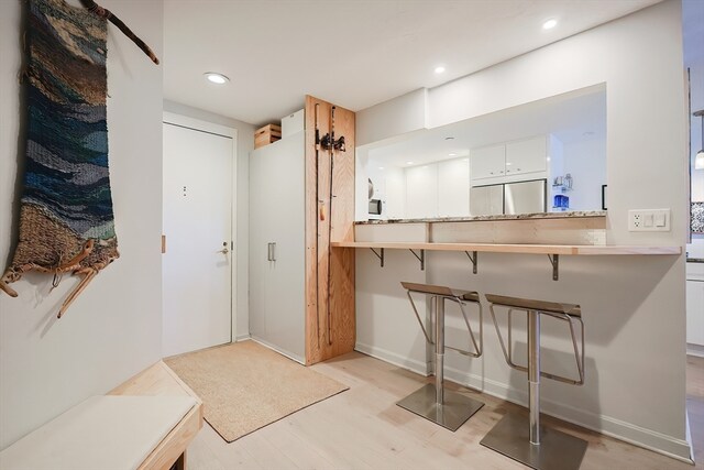 kitchen with kitchen peninsula, stainless steel built in refrigerator, light hardwood / wood-style flooring, and white cabinets